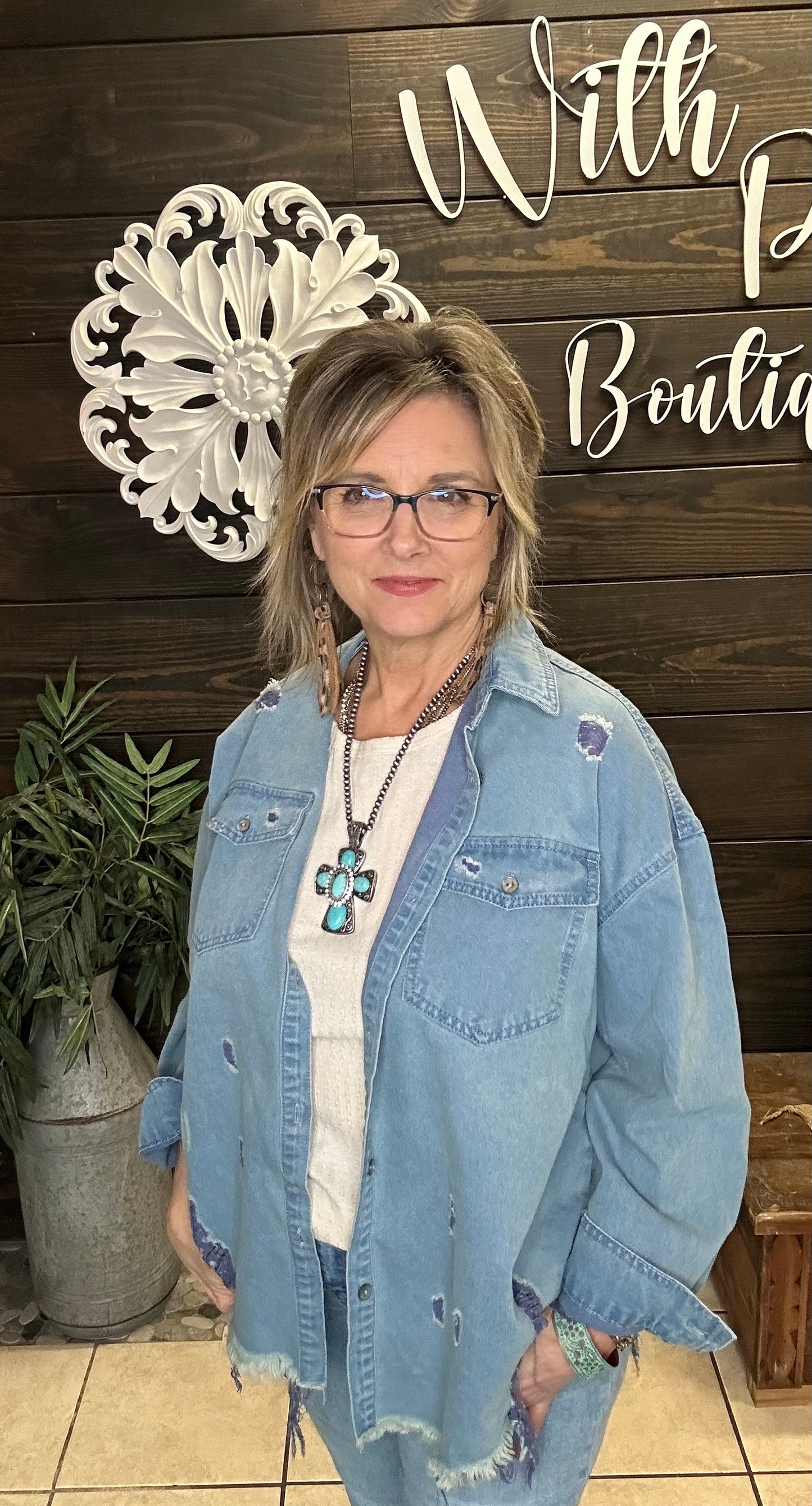 Woman wearing a denim jacket in front of a wooden wall with decorative elements