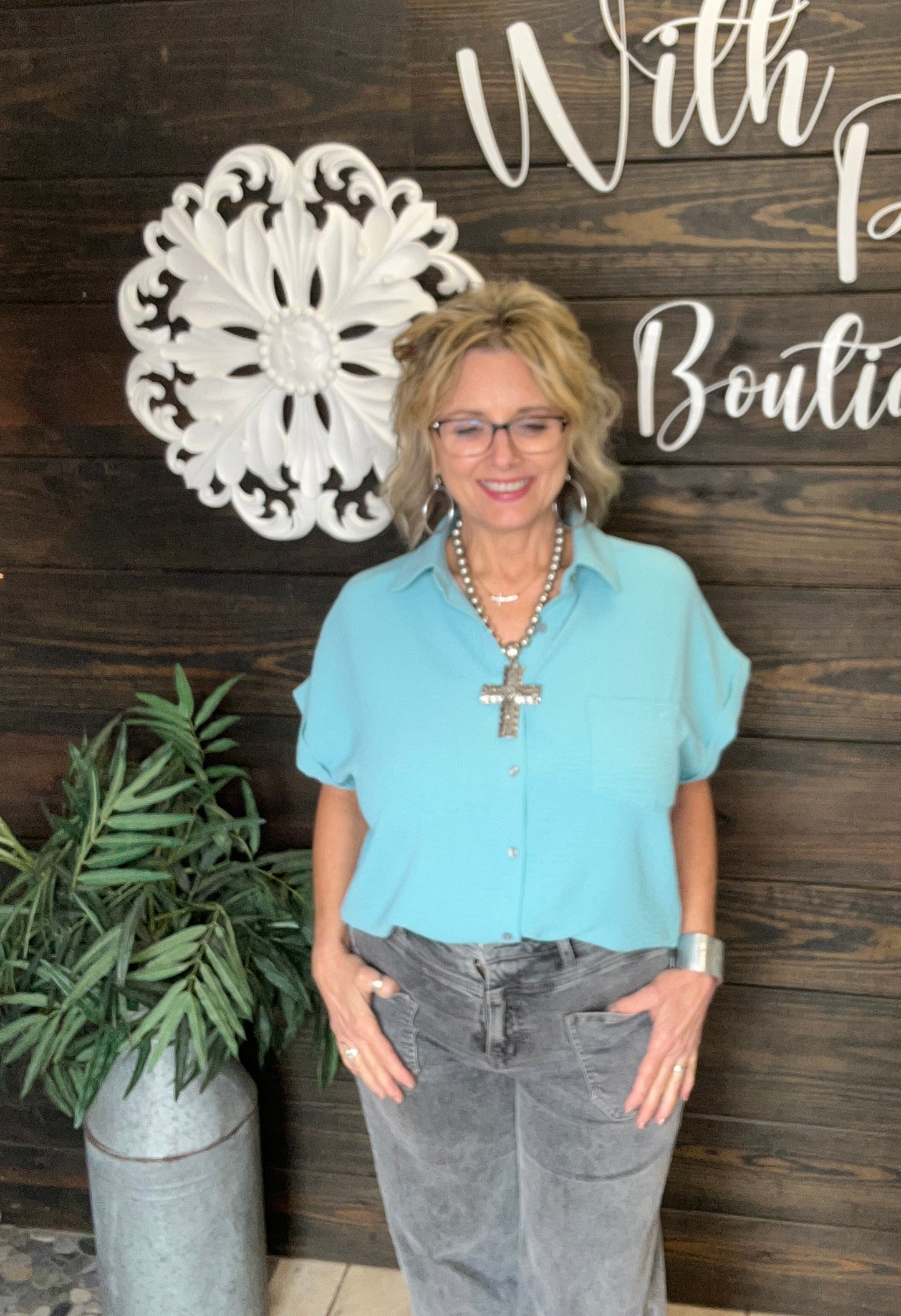 Teal colored relaxed fit button down with front pocket, hi low hem, side slit, air flow material, short sleeves with small, rolled cuff.