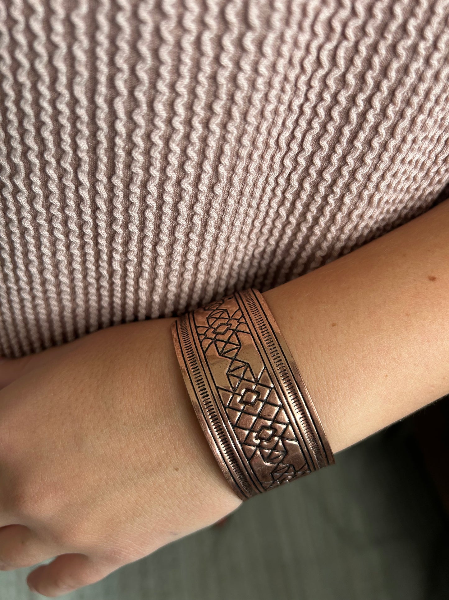 Copper bracelet on a wrist against a textured fabric background