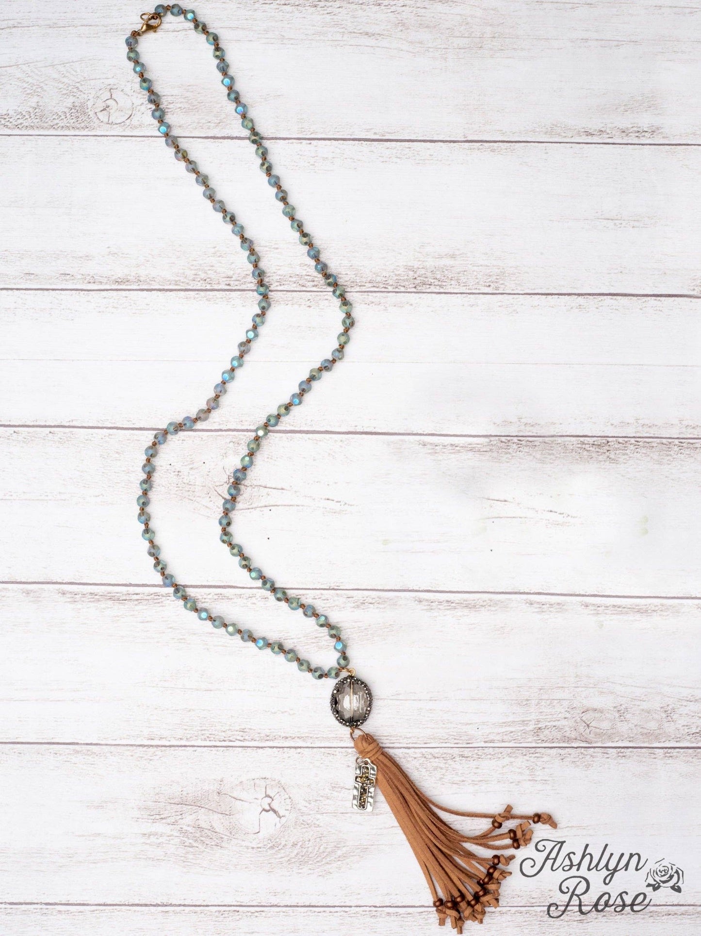 Necklace with tassel on a wooden surface, branded 'Ashlyn Rose'.