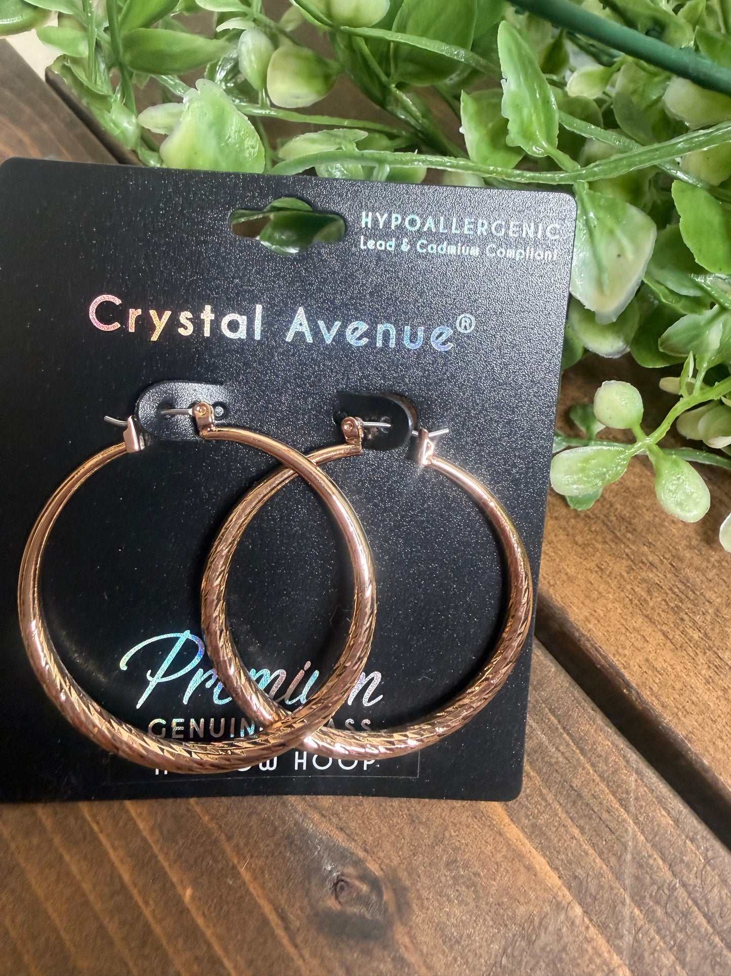 Gold hoop textured earrings on a jewelry card on a board with greenery
