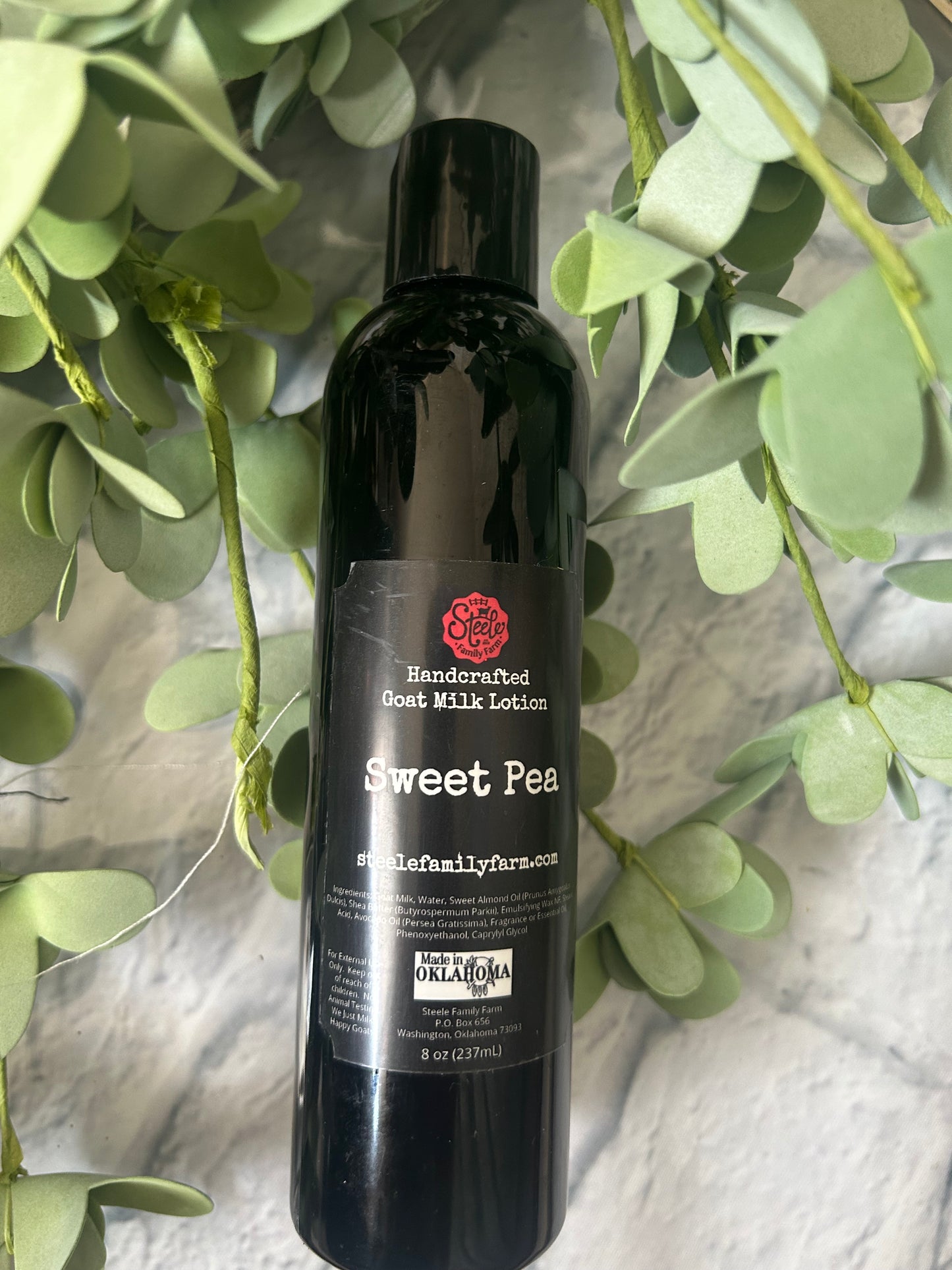Bottle of Sweet Pea Goat Milk Lotionon a surface with green leaves in the foreground
