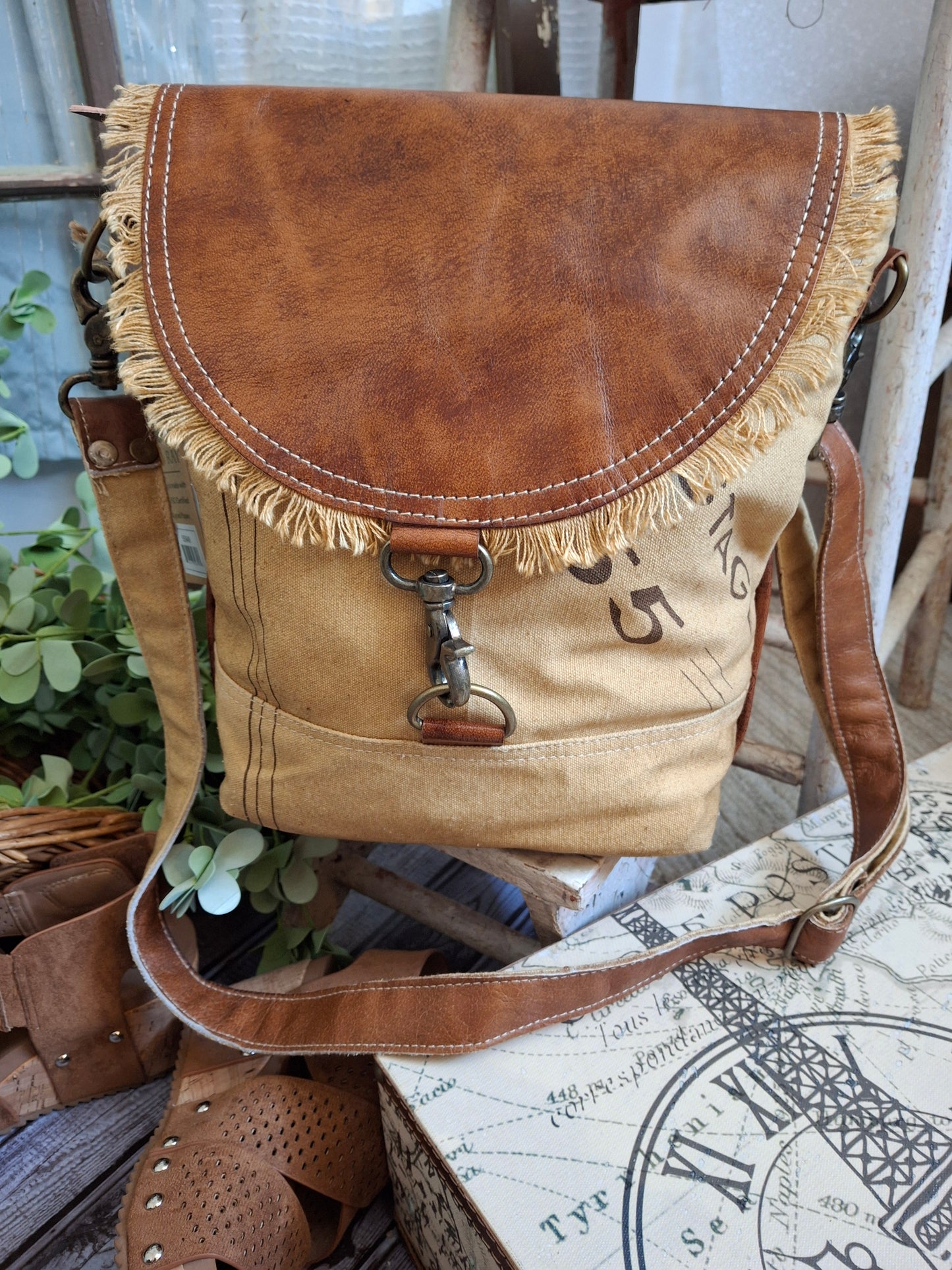 This stylish shoulder bag will add a vintage touch to your wardrobe! It has retro postage stamp lettering, and a fringe trimmed flap. It's super roomy with plenty of storage inside and out. It features a vintage blue and white stripe lining, three inside pockets, two outside pockets, and an adjustable shoulder strap.