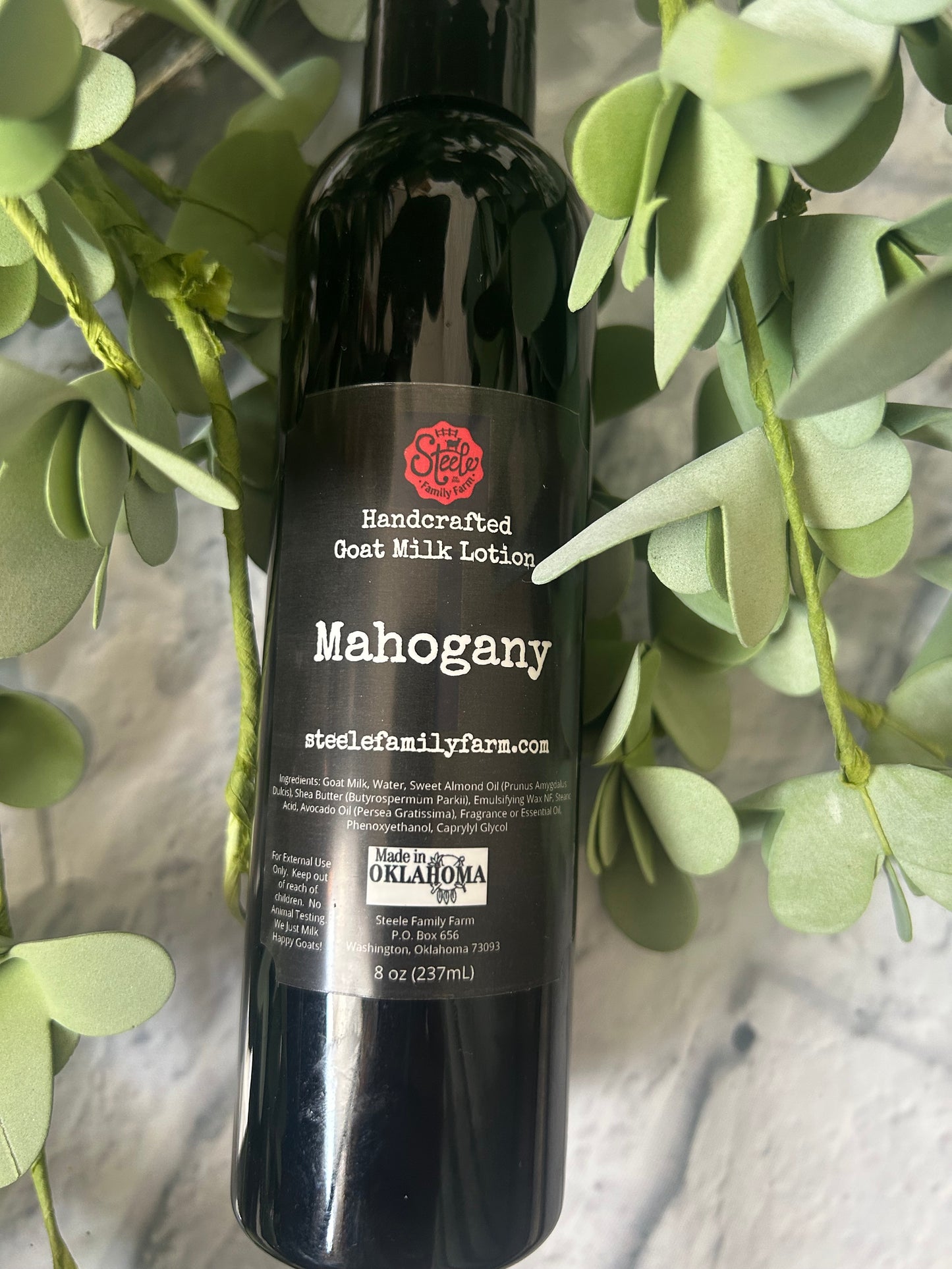 Bottle of Mahogany Goat Milk lotion with a green leafy background
