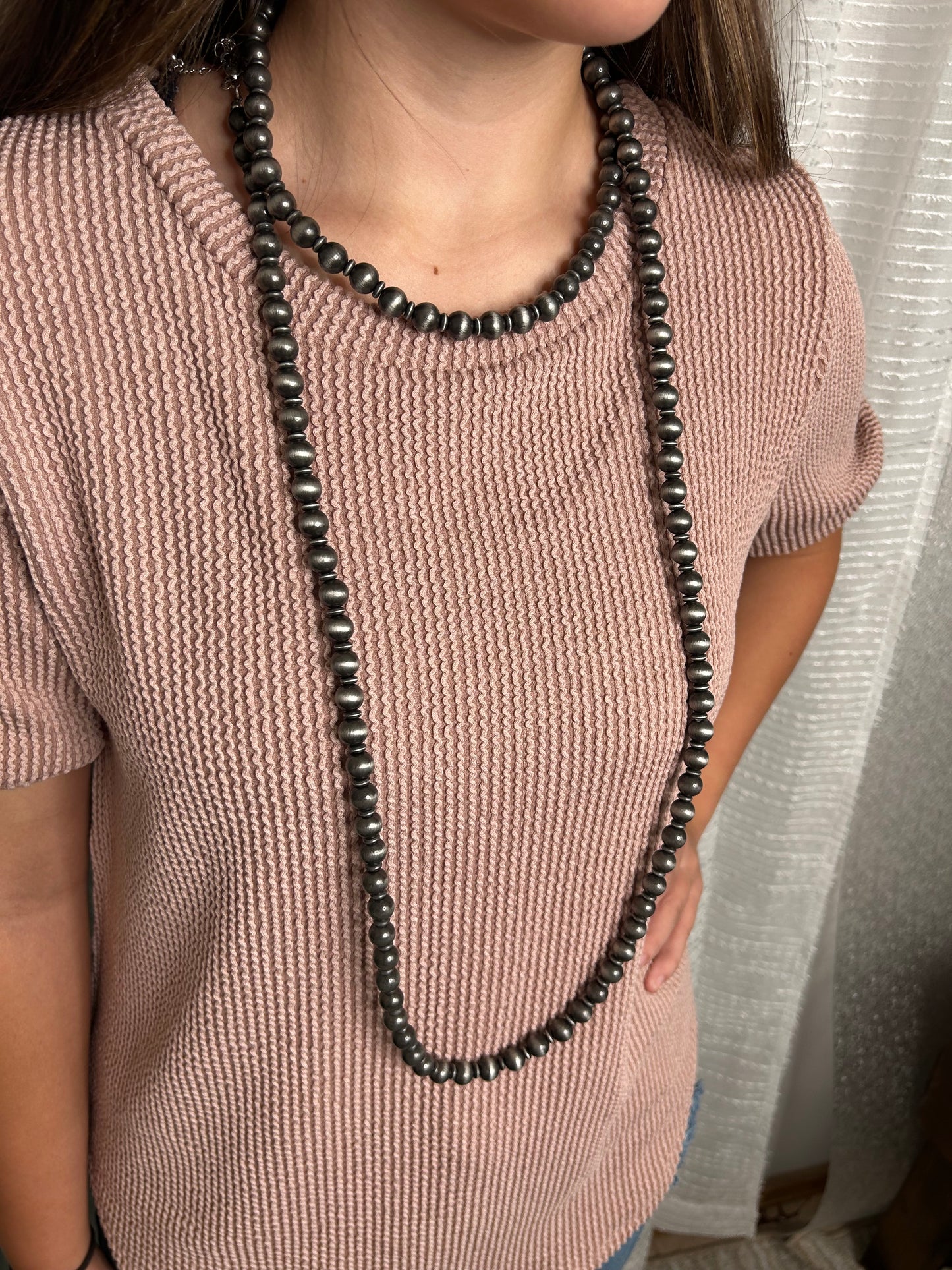 Person wearing a Navajo beaded necklace on a plain background