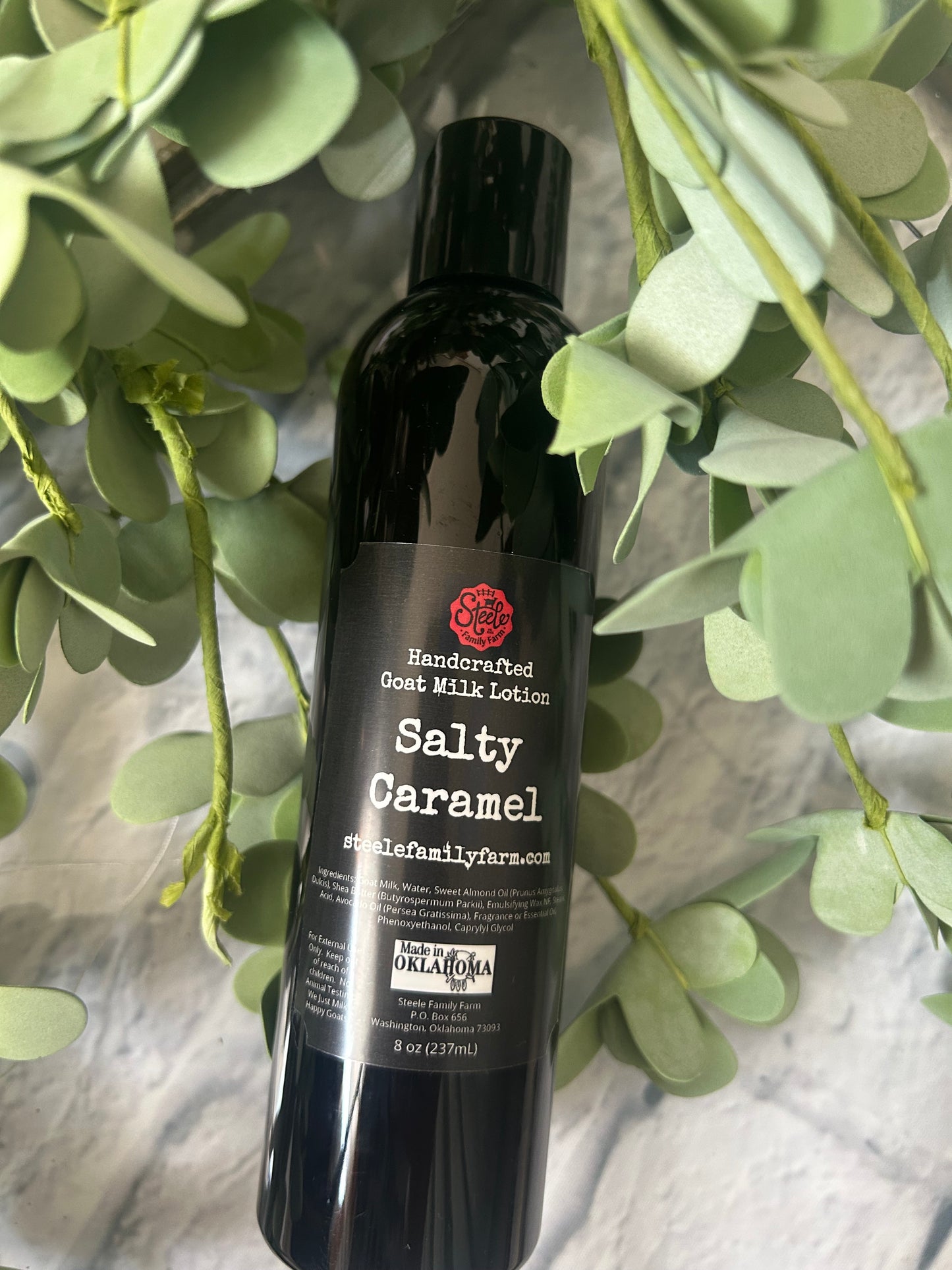 Bottle of Salty Caramel Goat Milk Lotion with green leaves in the background