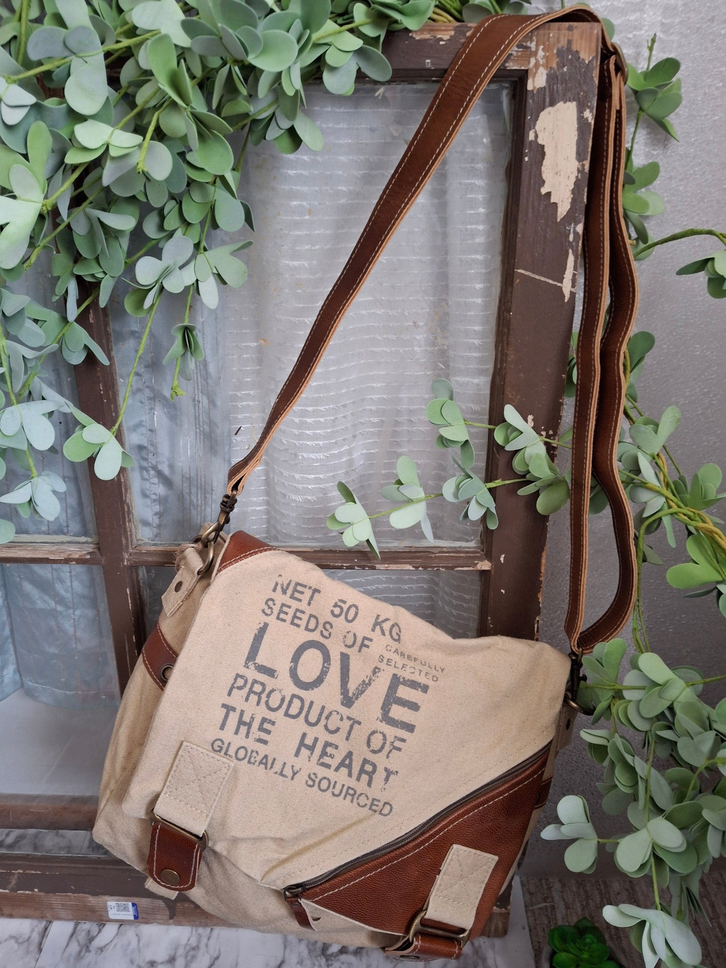 Discover a new way to carry your essentials with the Seeds Of Love Messenger Bag. This bag is multi-functional and will quickly become your workhorse accessory. It has ample storage and could easily be used to carry books, files, or even be used as a trendy diaper bag! The embossed inspirational message makes this bag truly unique. It features a vintage blue and white stripe lining, three inside pockets, one outside pocket and an adjustable shoulder strap.