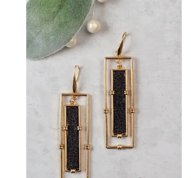 Gold-framed earrings with black stones on a light gray surface,