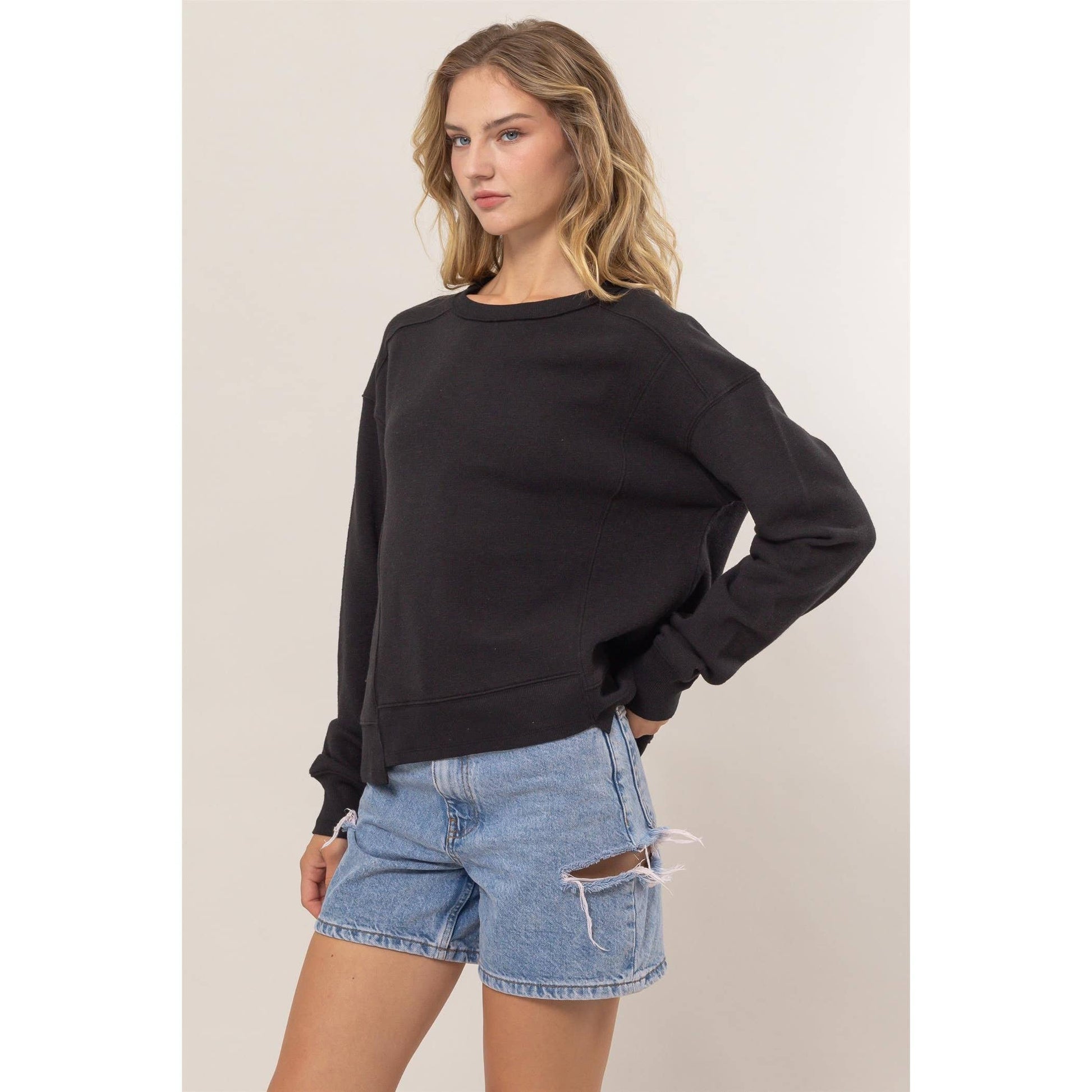 Woman wearing a black sweater and denim shorts on a plain background