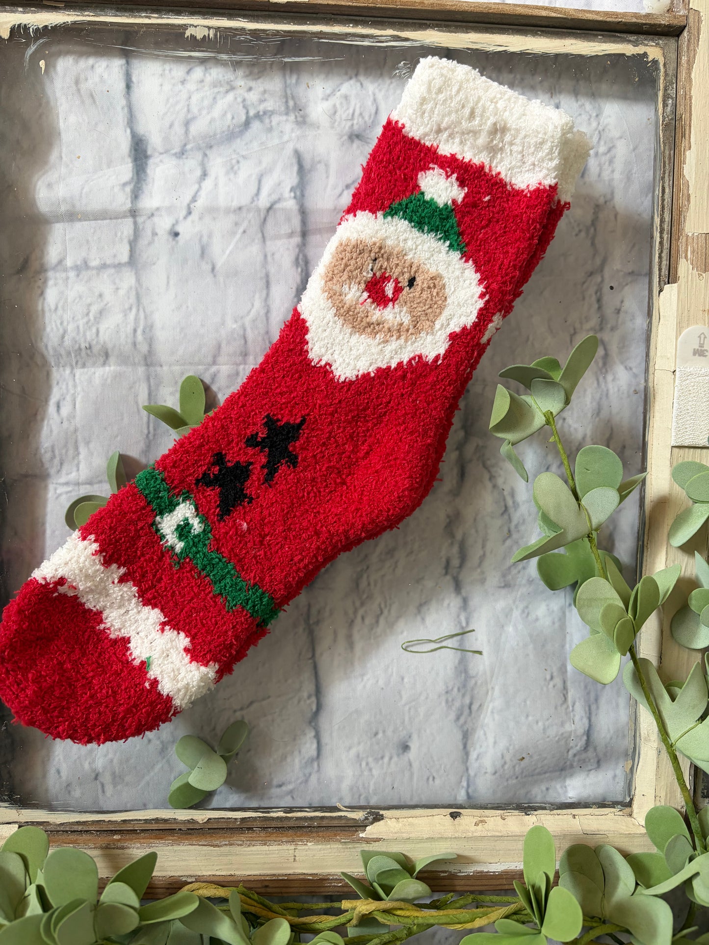 Red Christmas stocking with a Santa face design on a wooden surface with greenery.