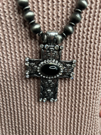 Decorative cross pendant with black gemstone on a textured beige fabric background