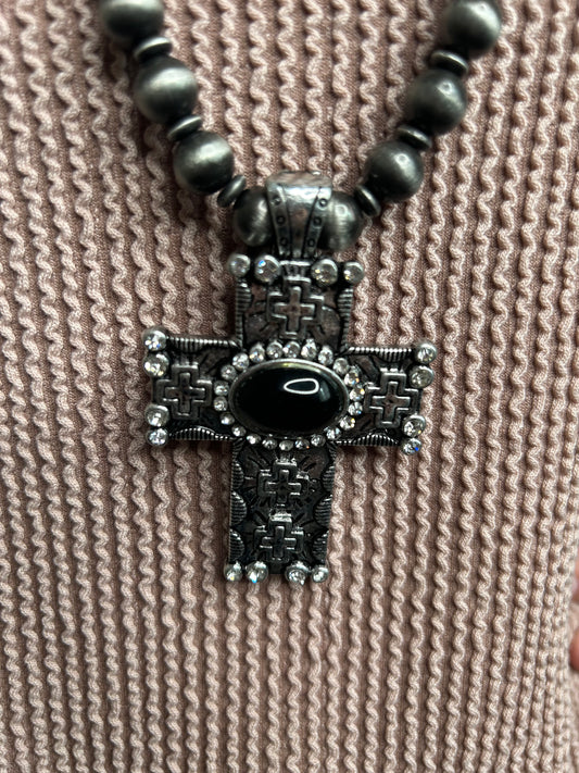 Decorative cross pendant with black gemstone on a textured beige fabric background