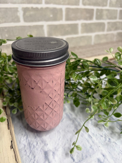 Pink textured coffee cup with black lid on a light gray surface with green plants.