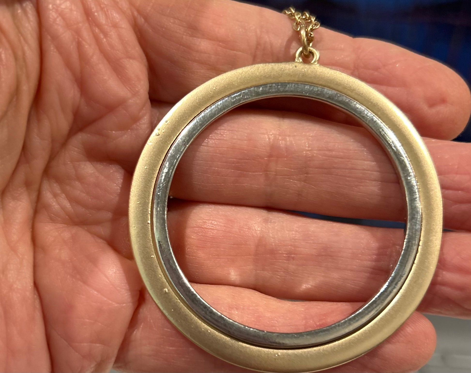 Gold and silver circular pendant held in a hand
