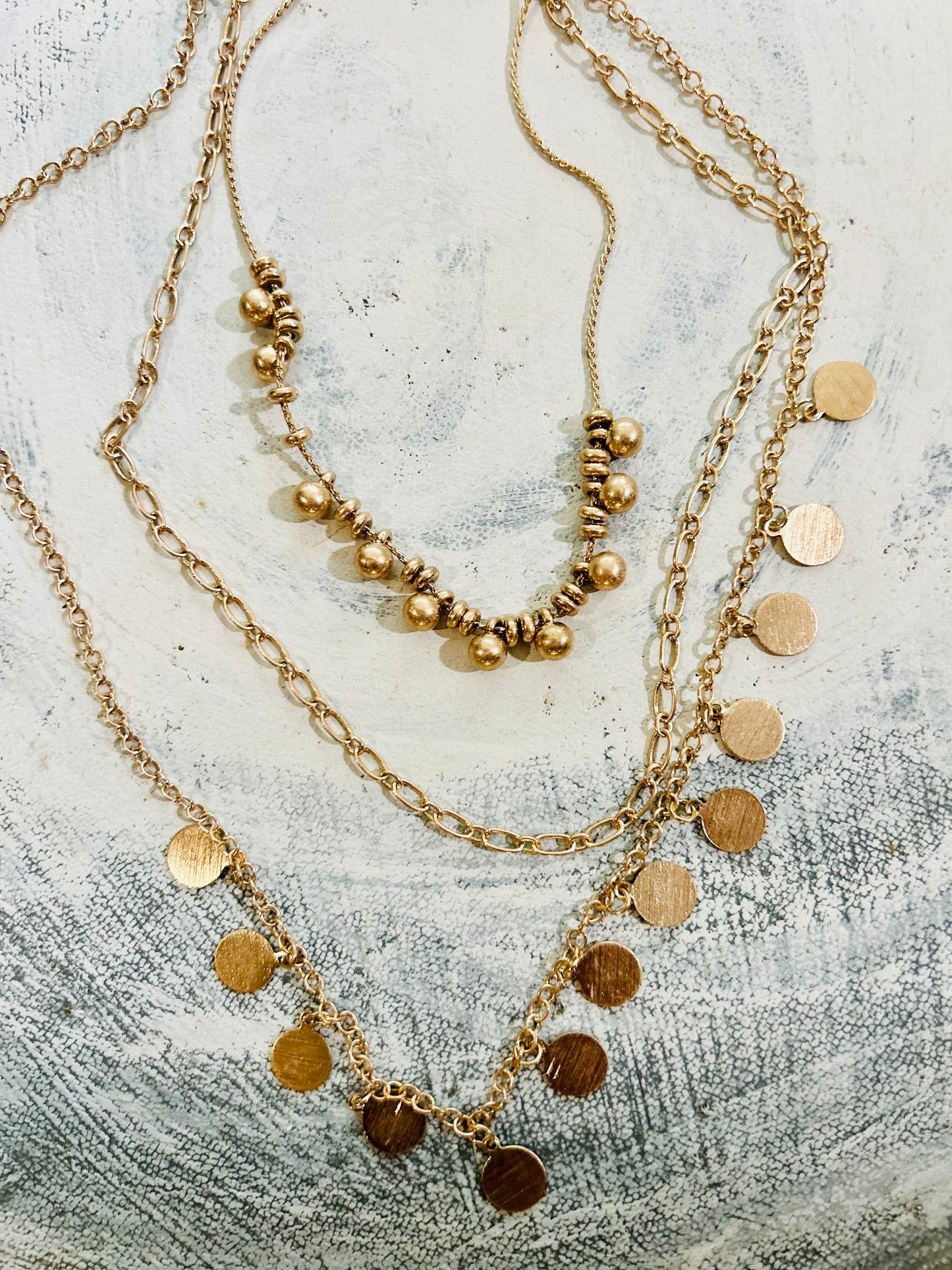 Three gold necklaces with beads and coins on a textured surface