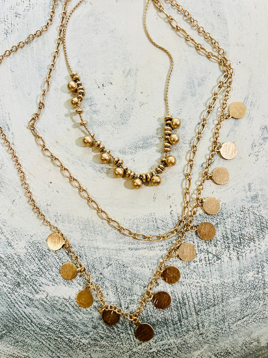 Three gold necklaces with beads and coins on a textured surface