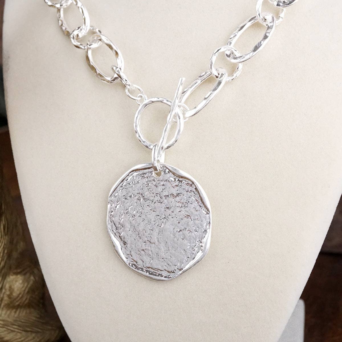 Silver necklace with a textured pendant on a mannequin.