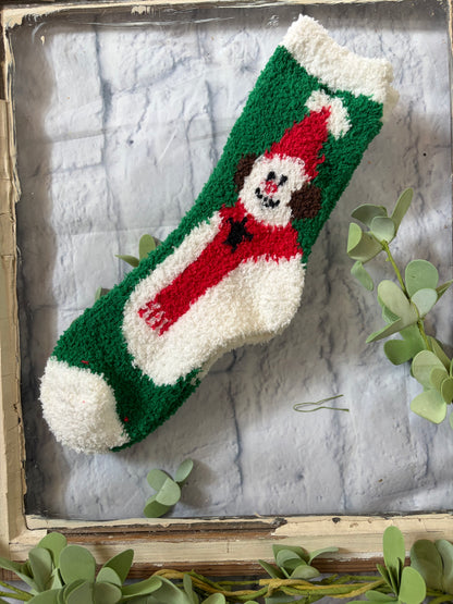 Knitted snowman-themed item on a textured surface with greenery