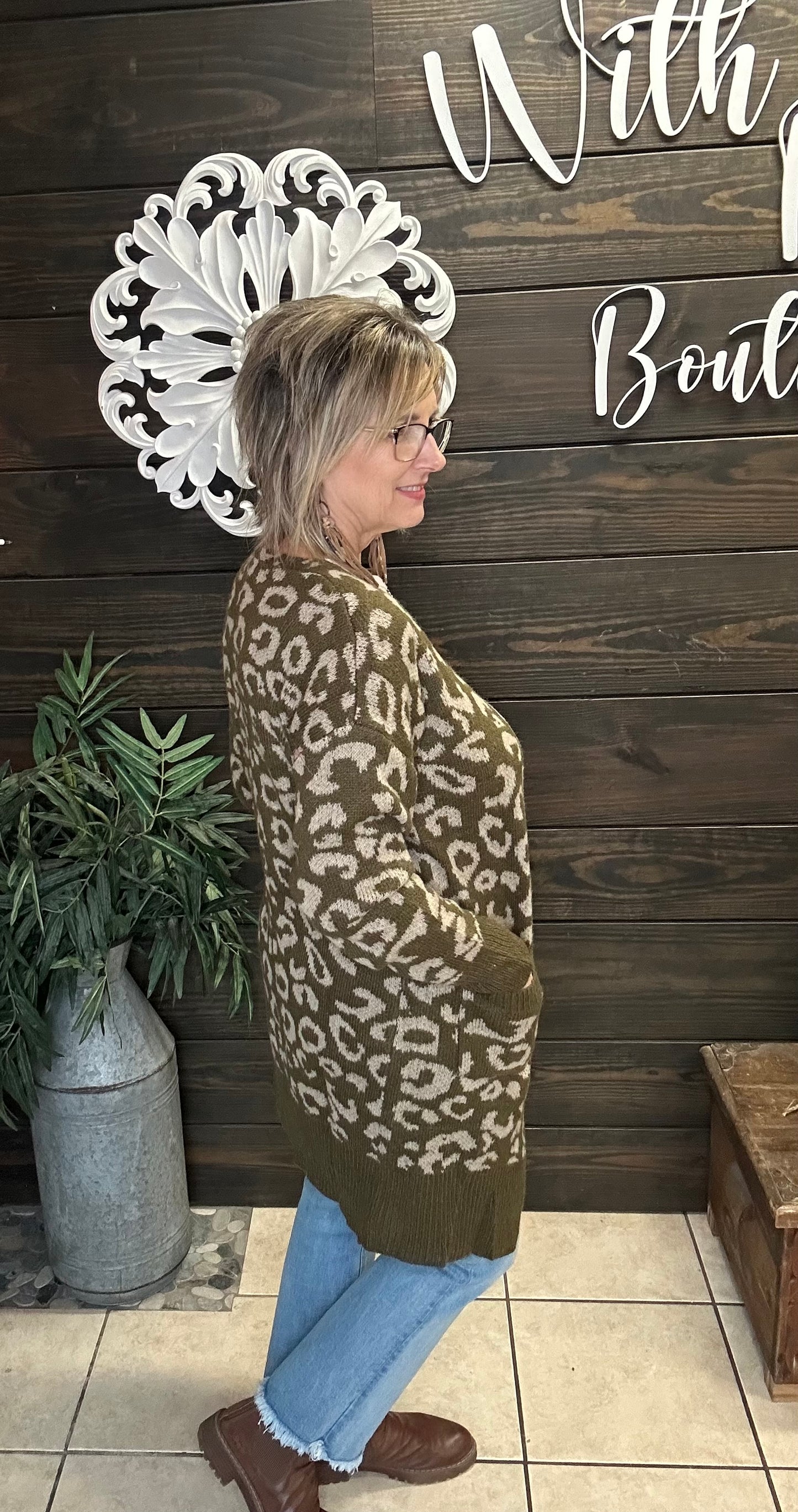 Woman wearing a leopard print cardigan in front of a wooden wall with decorative elements.