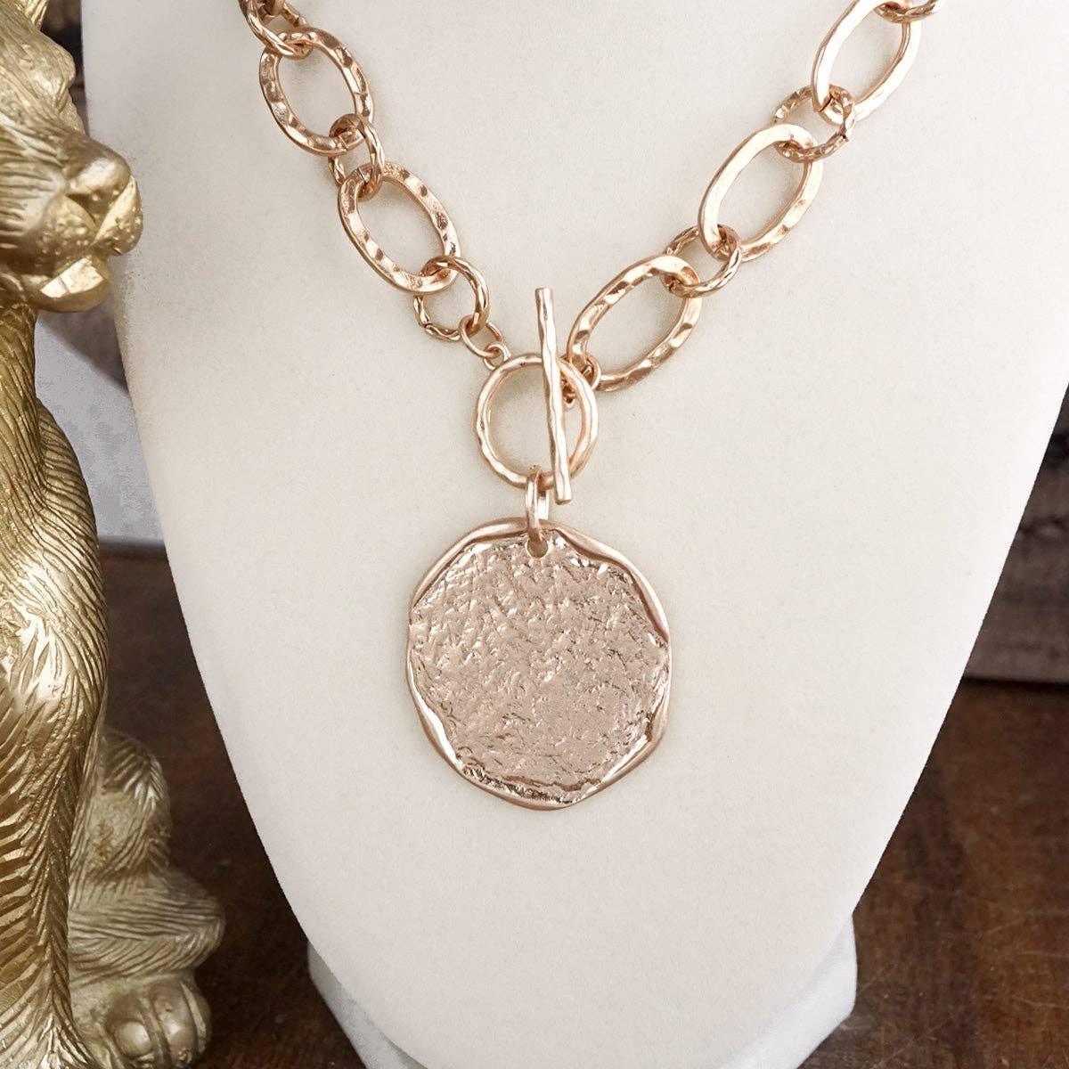 Gold necklace with a round pendant on a white stand.