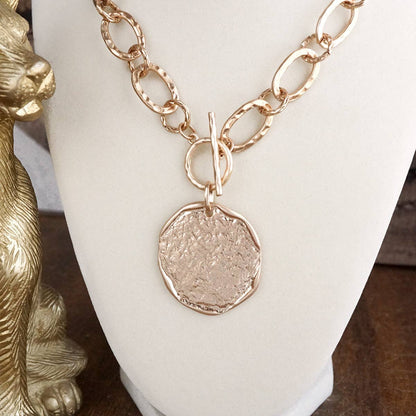 Gold necklace with a round pendant on a white stand.