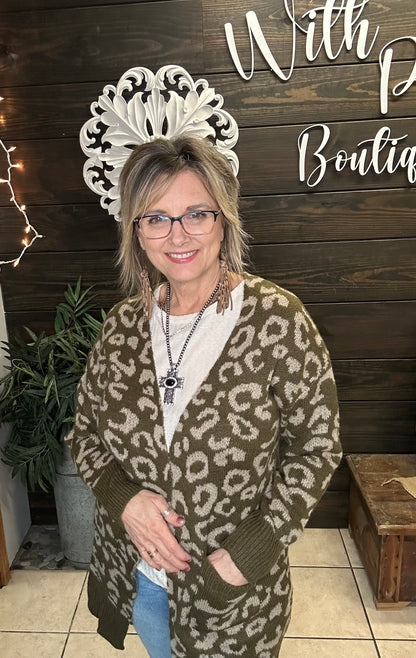 Woman wearing a leopard print cardigan in front of a wooden wall with decorative elements.