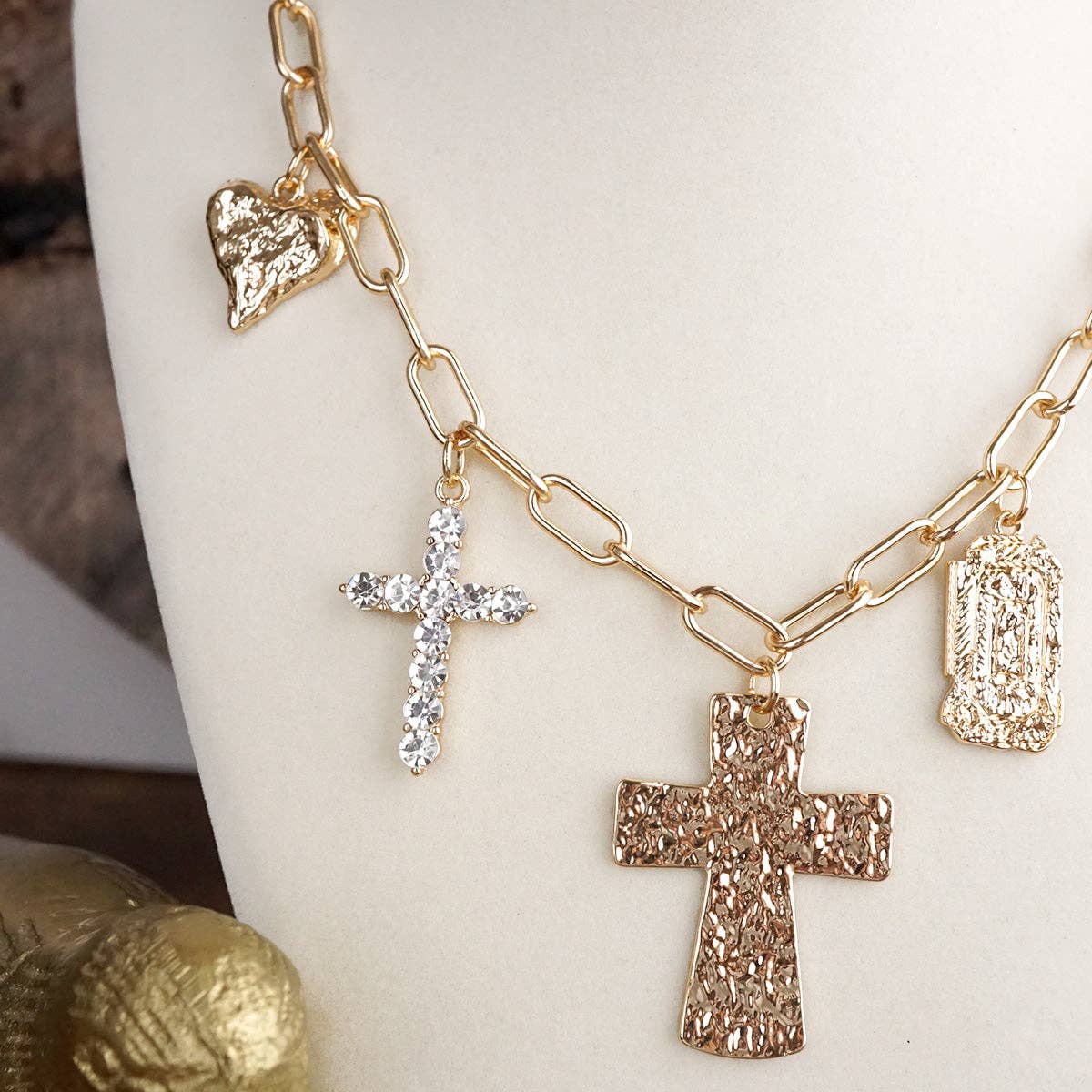 Gold necklace with various charms including crosses and a heart on a white stand.