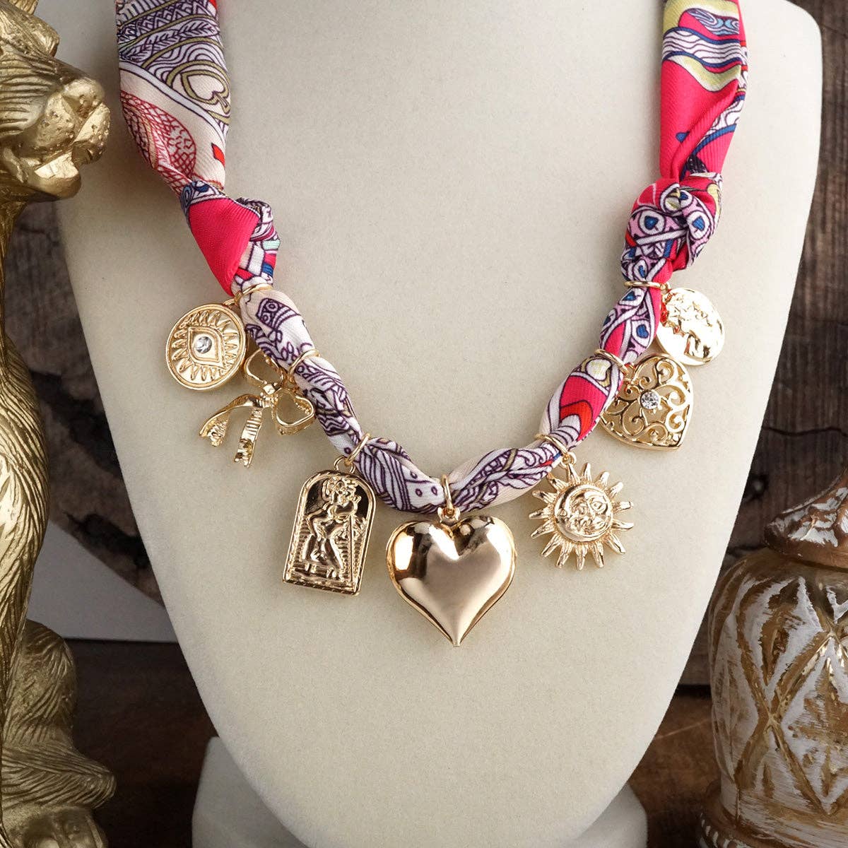 Necklace with gold charms and a patterned fabric strap on a mannequin bust.