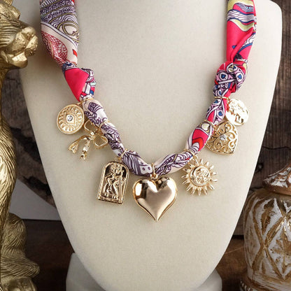 Necklace with gold charms and a patterned fabric strap on a mannequin bust.