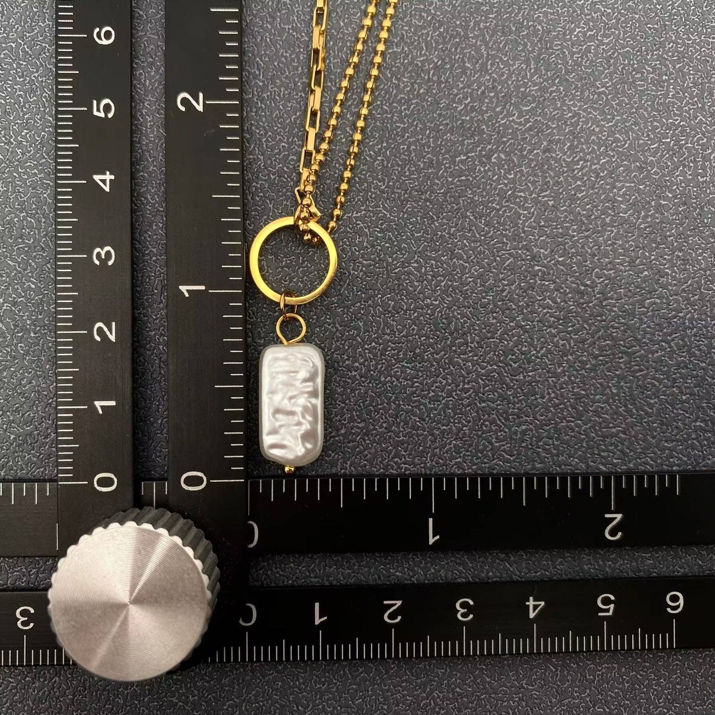 Gold necklace with a pendant on a black surface with a ruler for scale.