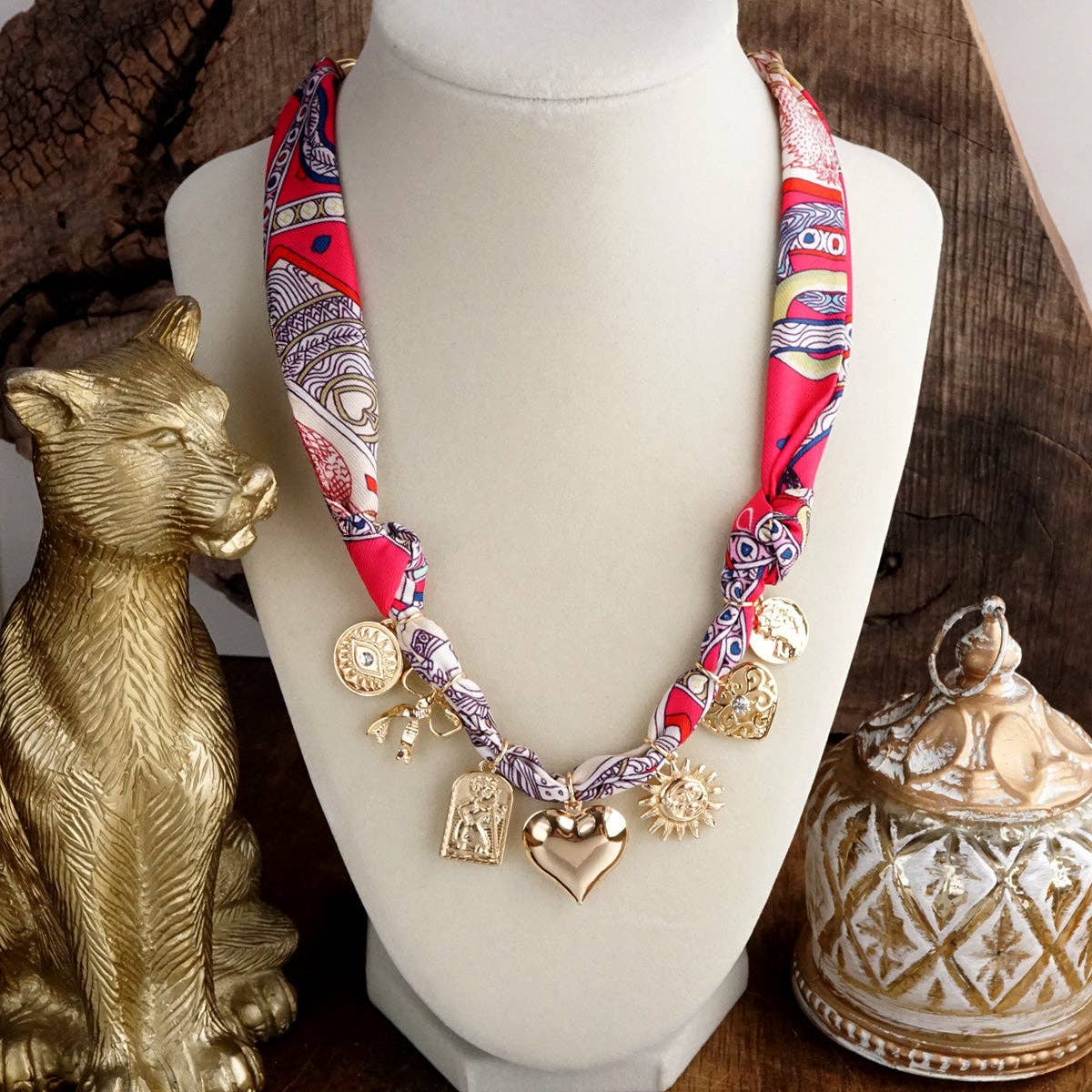Necklace with colorful fabric strap and charms on a mannequin bust, surrounded by decorative items.