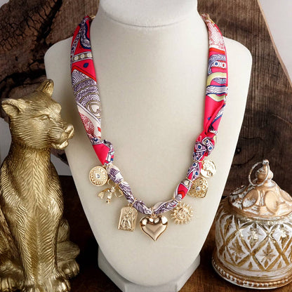 Necklace with colorful fabric strap and charms on a mannequin bust, surrounded by decorative items.