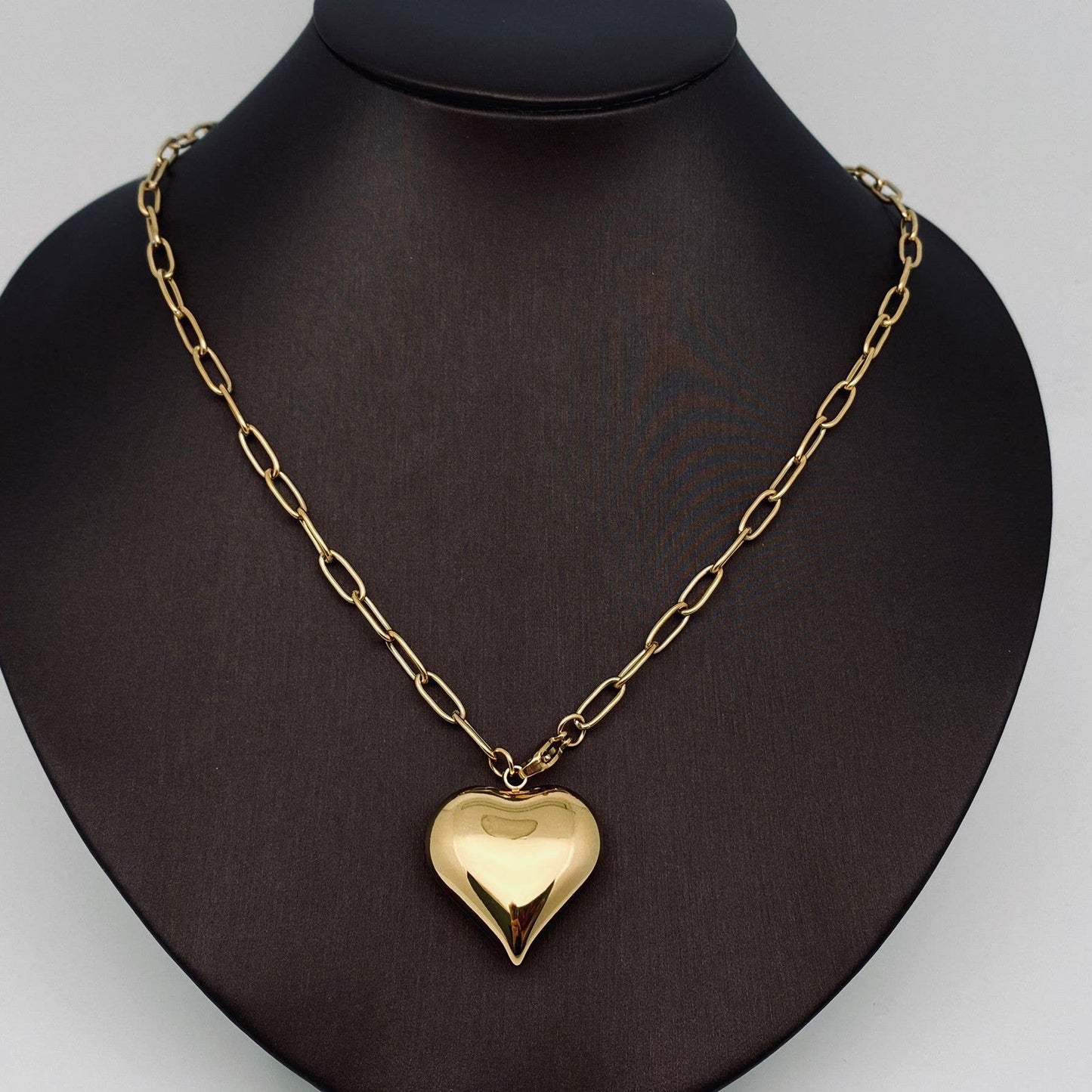 Gold heart-shaped pendant necklace on a black mannequin bust.