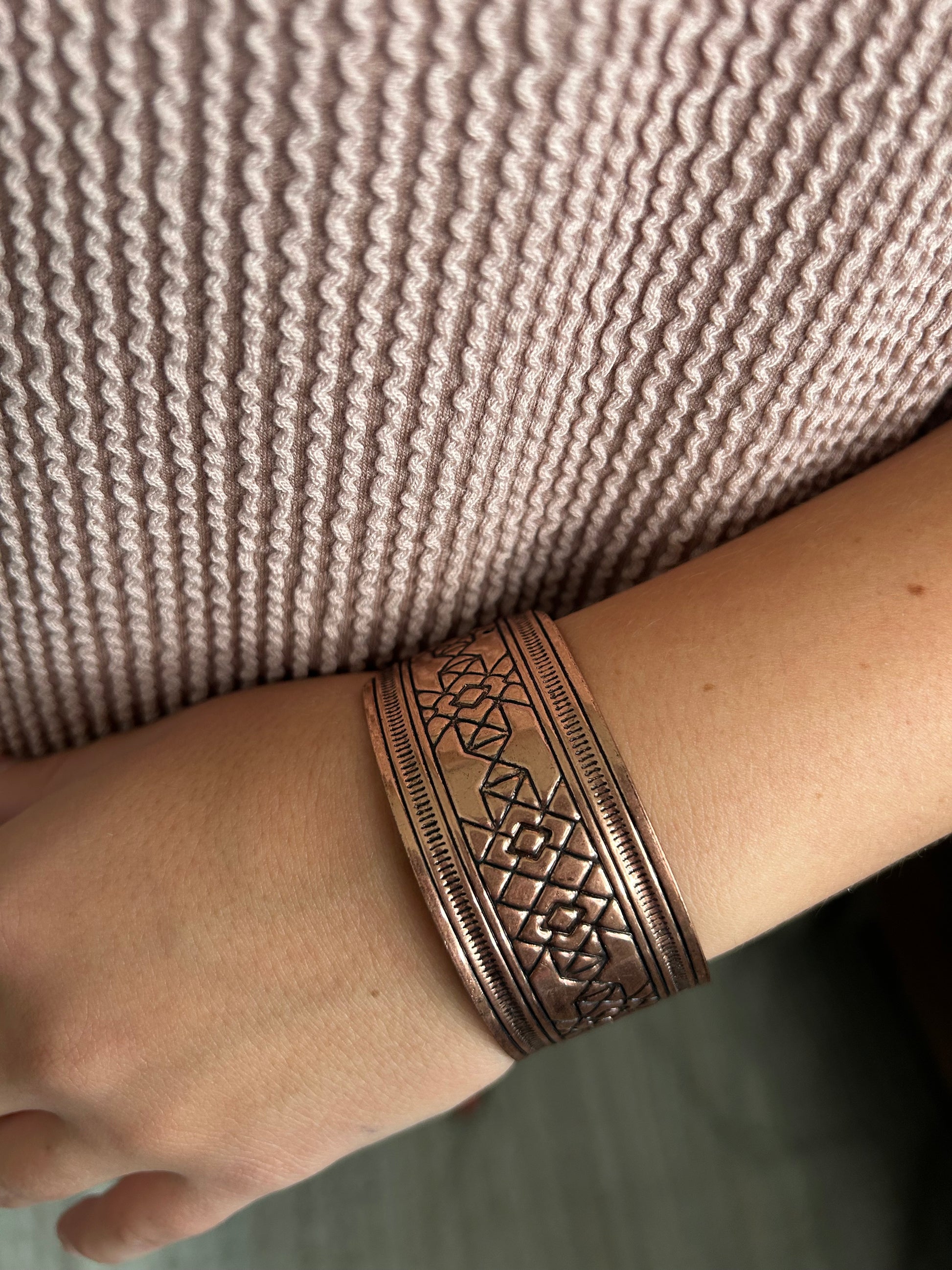 Copper bracelet on a wrist against a textured fabric background