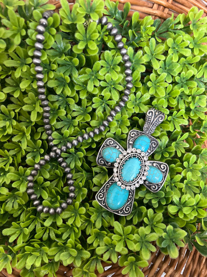 Turquoise cross necklace on green leaves