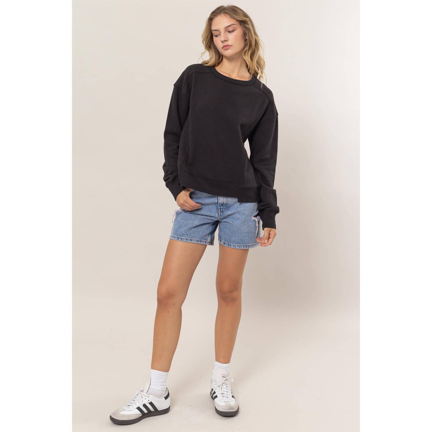 Woman wearing a black sweatshirt, blue shorts, and white sneakers on a beige background