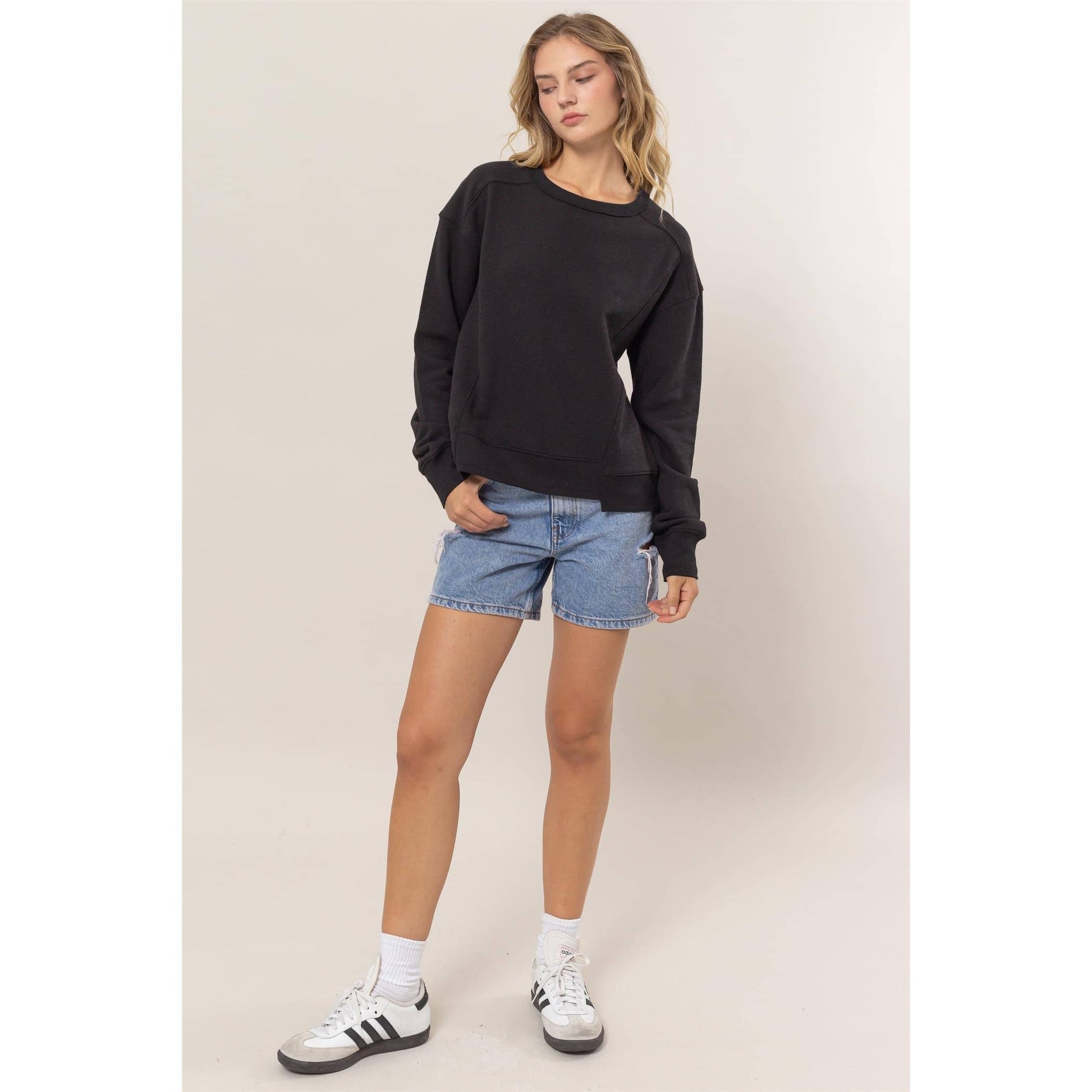 Woman wearing a black sweatshirt, blue shorts, and white sneakers on a beige background