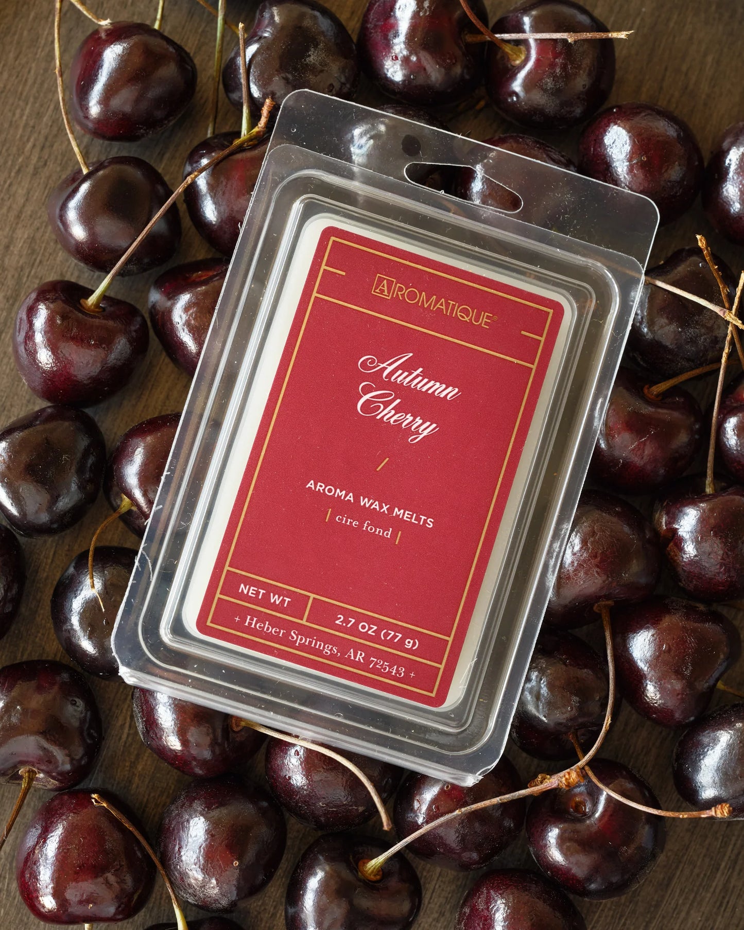 Aromatique Autumn Cherry wax melt package surrounded by cherries on a wooden surface