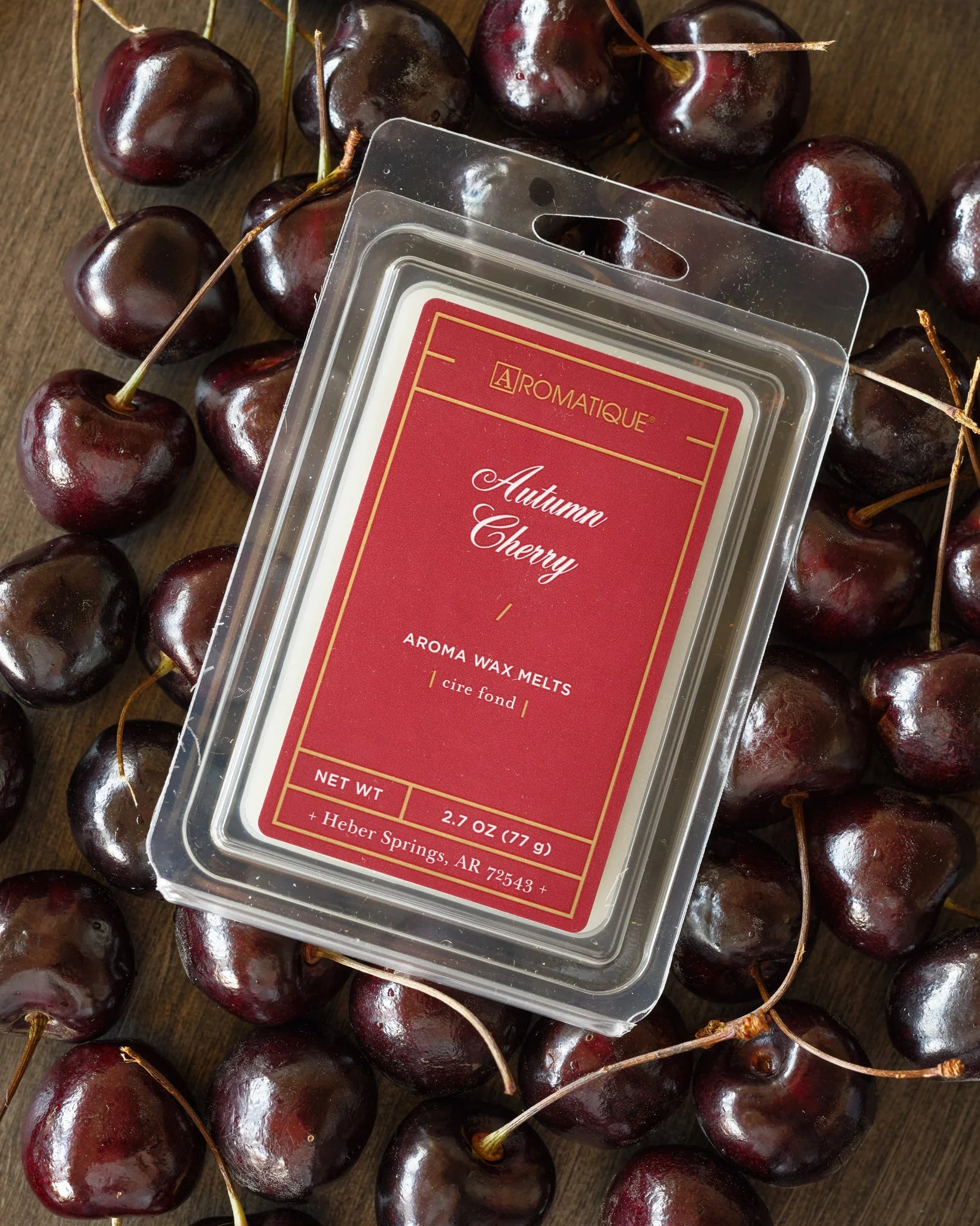 Aromatique Autumn Cherry wax melt package surrounded by cherries on a wooden surface