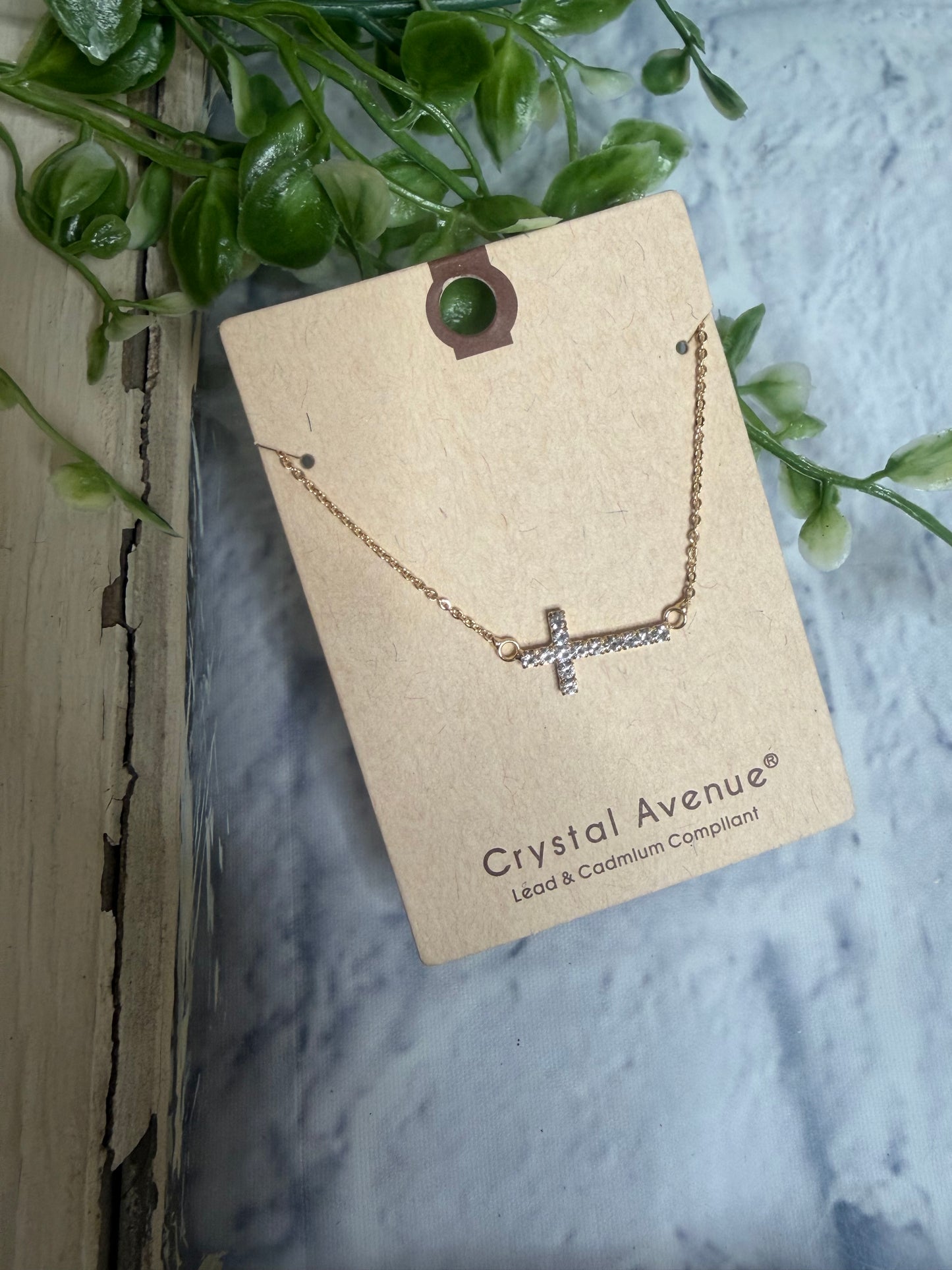 Necklace with a cross pendant on a 'Crystal Avenue' card with greenery in the background