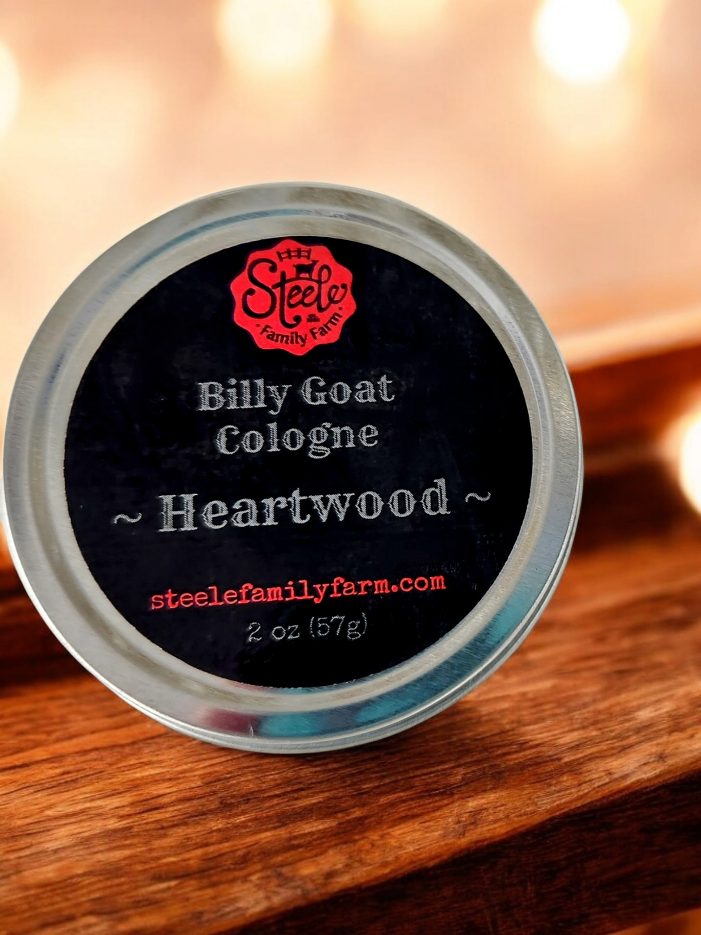 Container of Billy Goat Cologne Heartwood by Steele Family Farm on a wooden surface with blurred lights in the background.