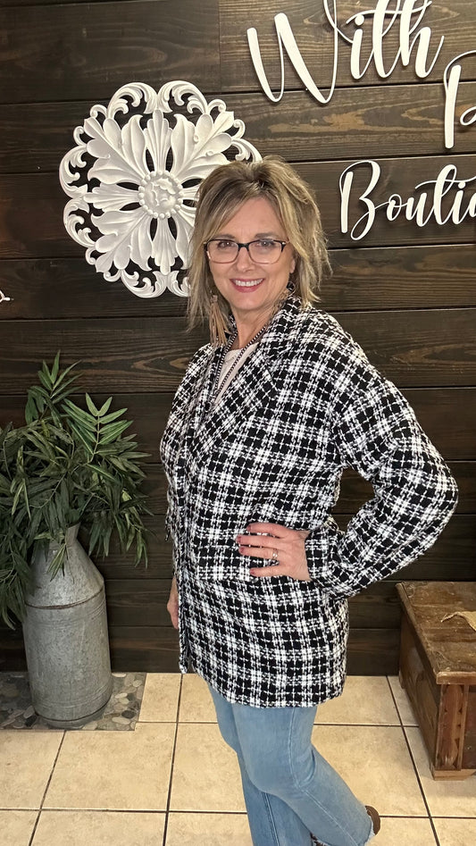 Woman wearing a black and white checkered jacket in front of a wooden wall with decorative elements.