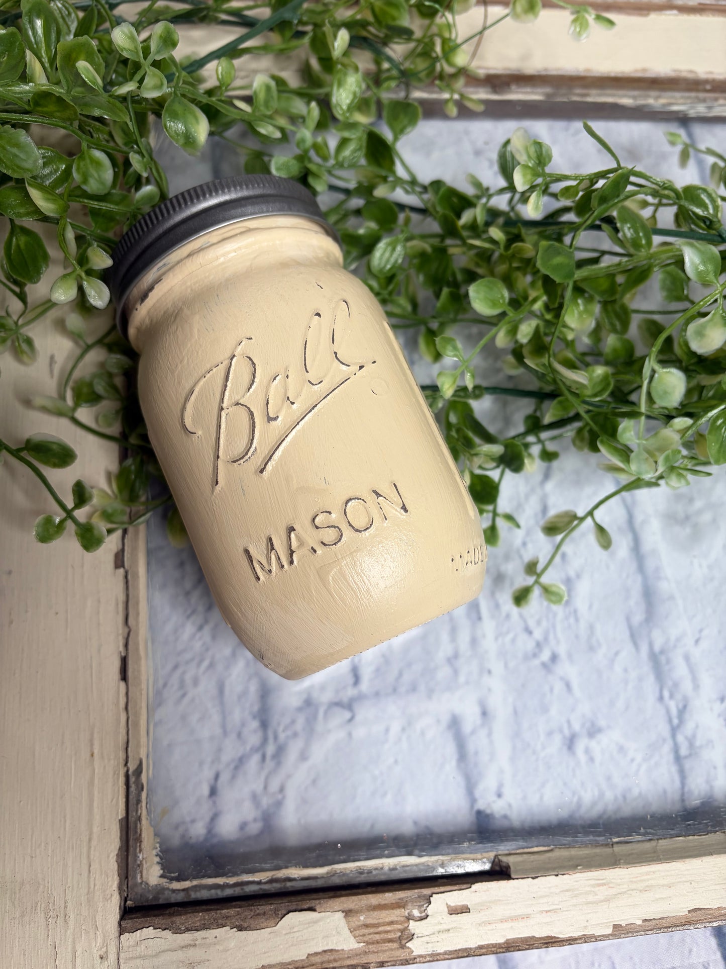 Mason jar lid with 'Ball' branding on a wooden surface with plants.