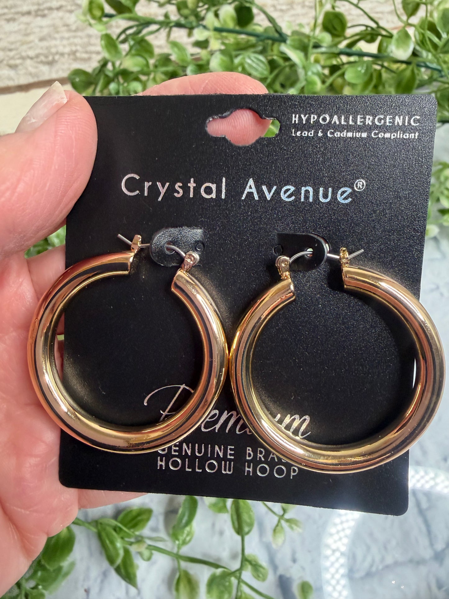 Gold hoop earrings on a Crystal Avenue card held by a hand with a natural background.