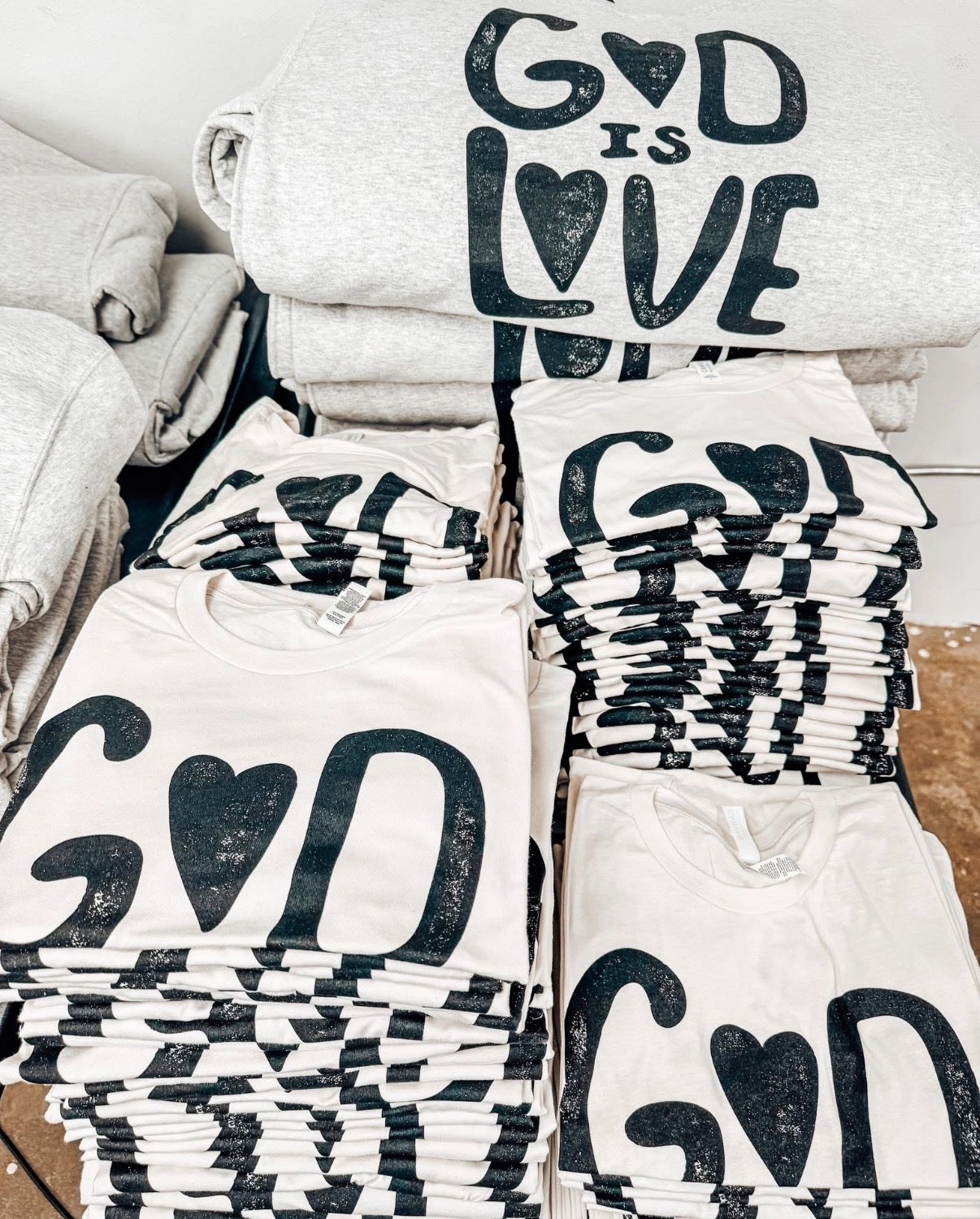 Stacks of t-shirts with 'God is Love' text on a white surface