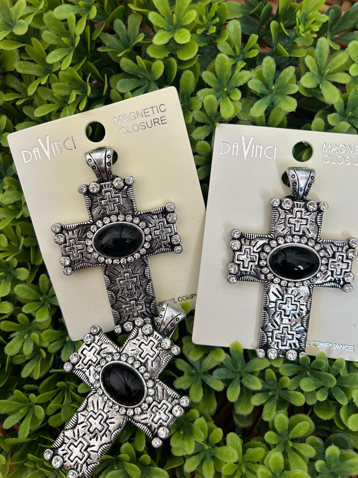 Silver cross-shaped pendantswith black centers on white cards against a green leafy background