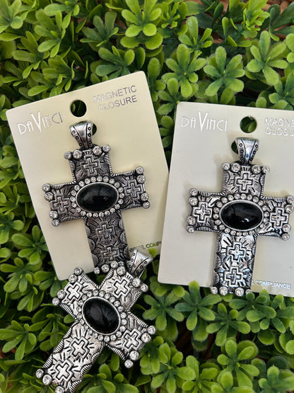 Silver cross-shaped pendantswith black centers on white cards against a green leafy background