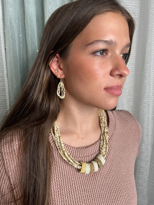 Woman wearing a gold necklace and earrings on a neutral background