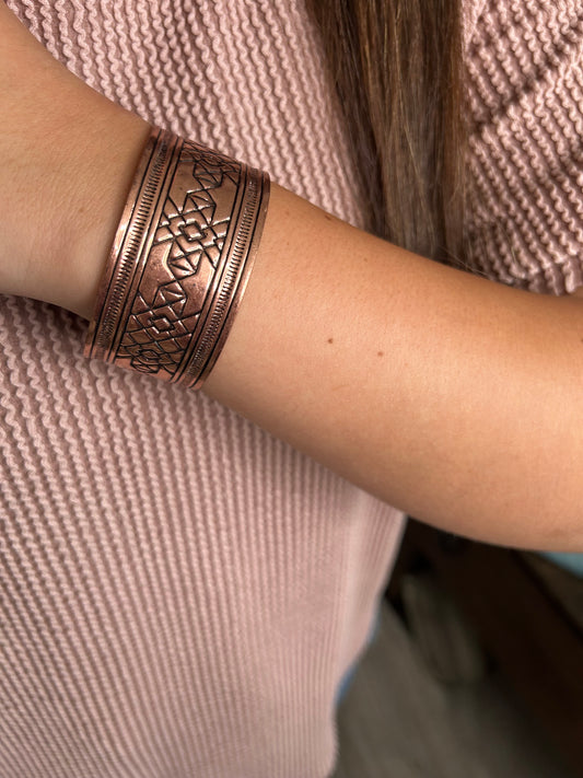 Copper bracelet with intricate design on a wrist against a textured fabric background