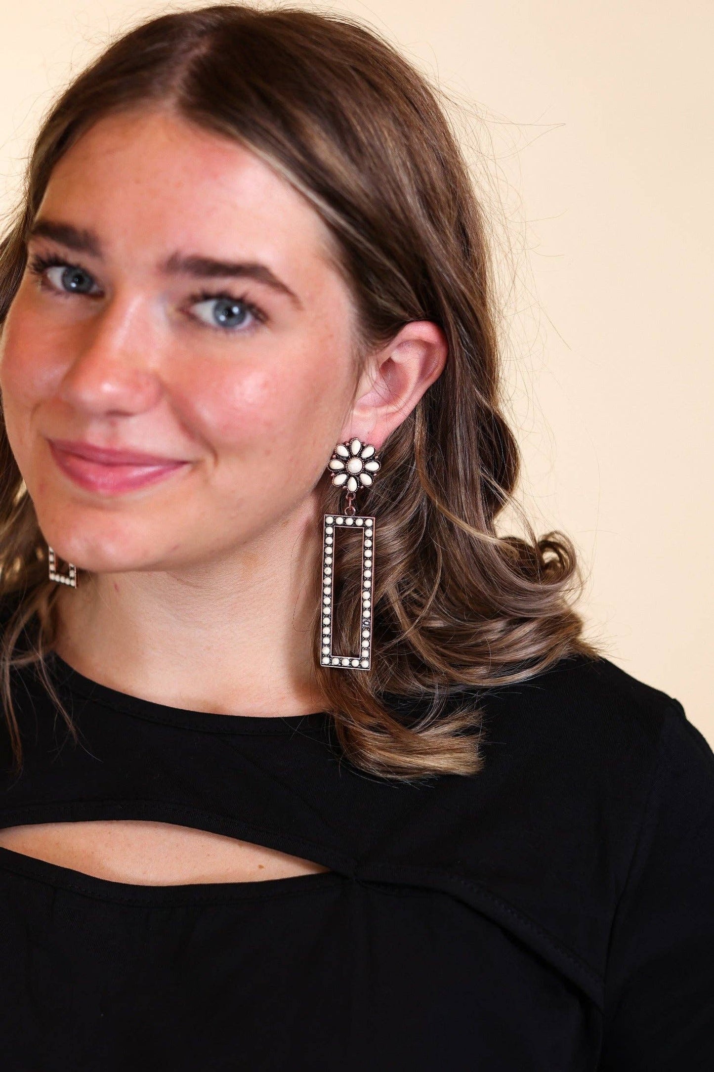 Woman wearing large, ornate copper and cream earrings against a plain background